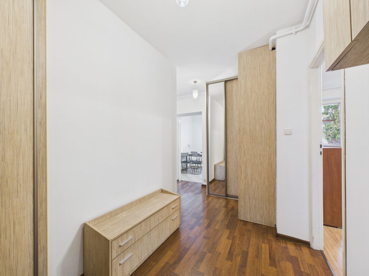 Hallway with white walls, wood floor, and light wood storage units along the left and at the far end.