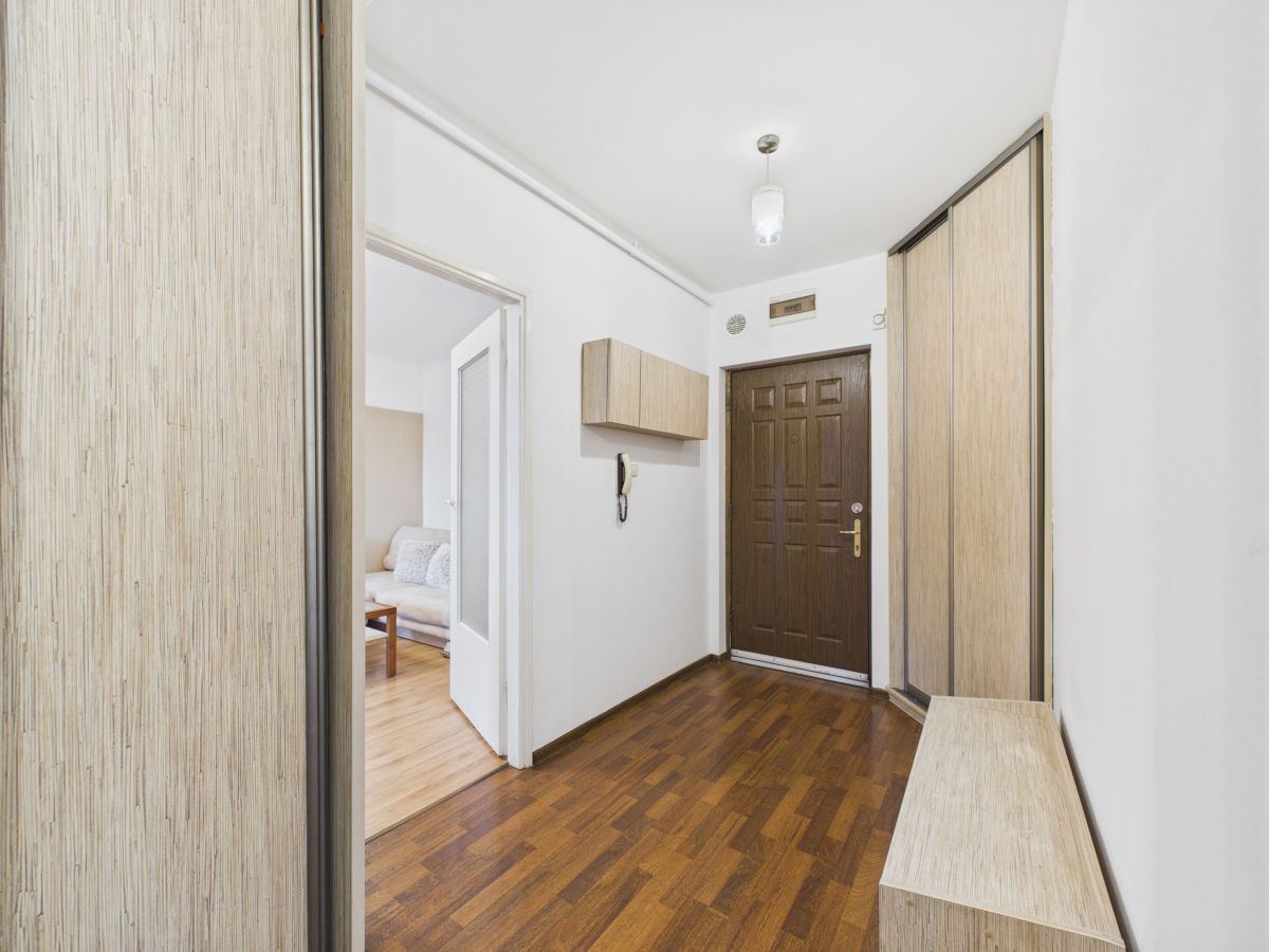 Entry hall with a dark brown front door, light wood storage along the right, and a bench; view toward the living room doorway.