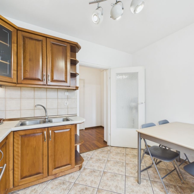 Wooden kitchen with brown cabinets, tiled backsplash, double sink, and a red coffee machine on the counter beside a dining table with chairs.