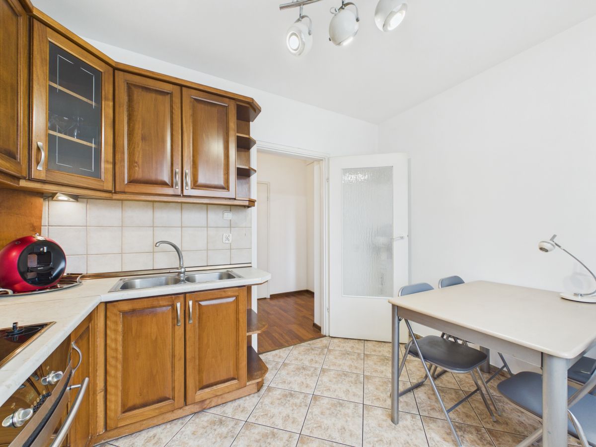 Wooden kitchen with brown cabinets, tiled backsplash, double sink, and a red coffee machine on the counter beside a dining table with chairs.