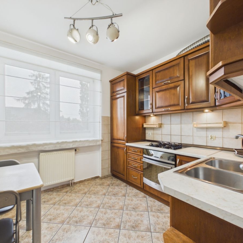 Kitchen with dark wood cabinets, gas stove and oven, stainless sink, and window with blinds.