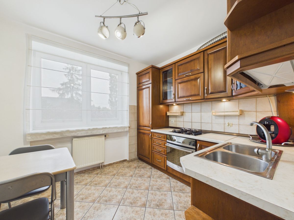 Kitchen with dark wood cabinets, gas stove and oven, stainless sink, and window with blinds.