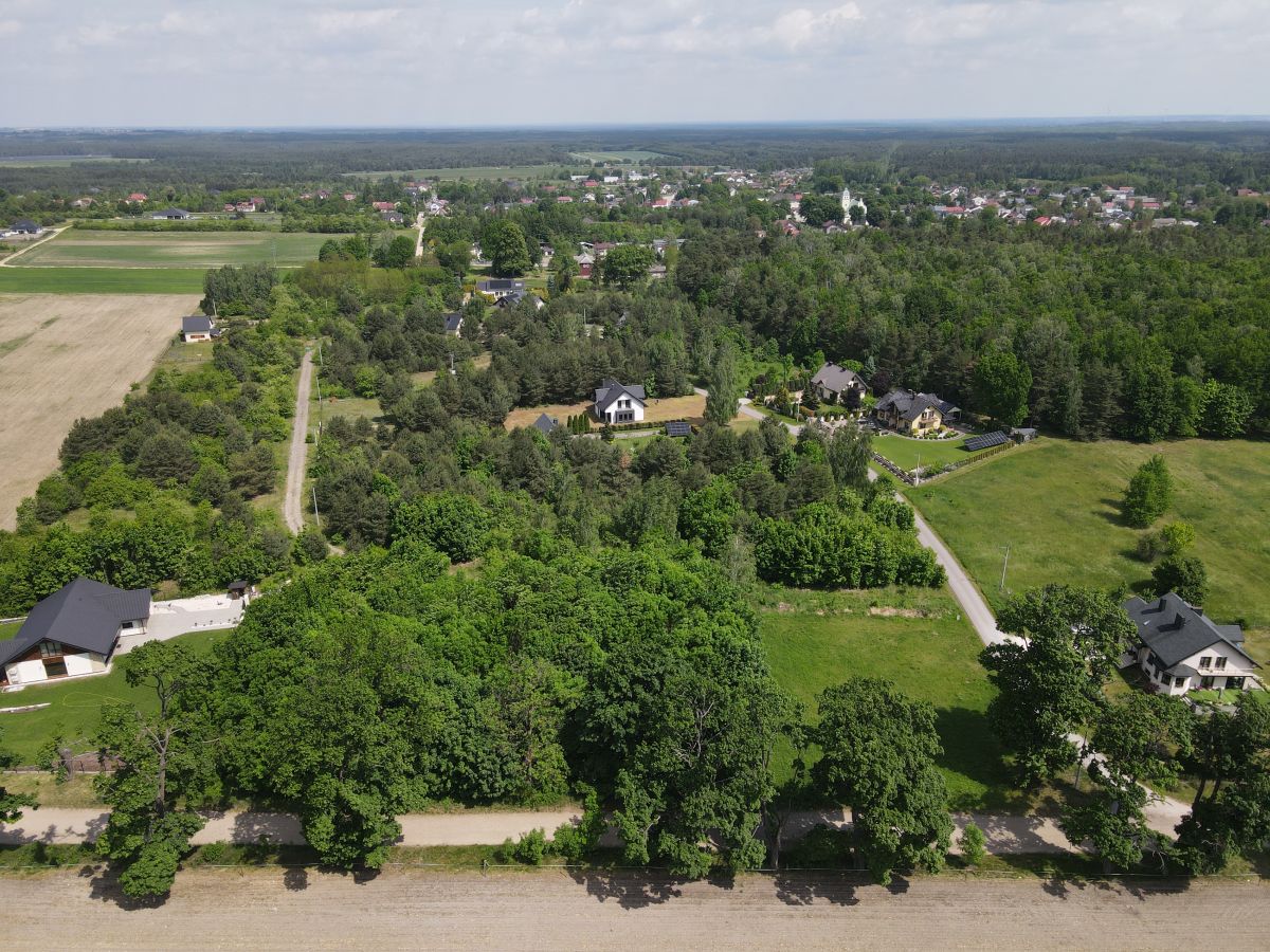 Aerial view of a rural neighborhood with dense trees, winding roads, and scattered houses amid fields and farmland.