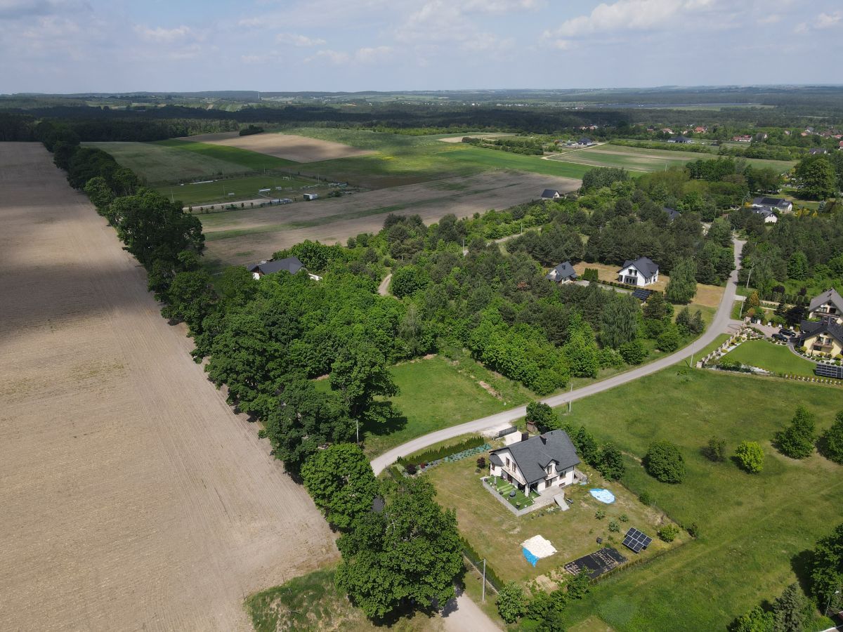 Aerial view of a rural landscape with fields, trees, and scattered houses along a winding road.