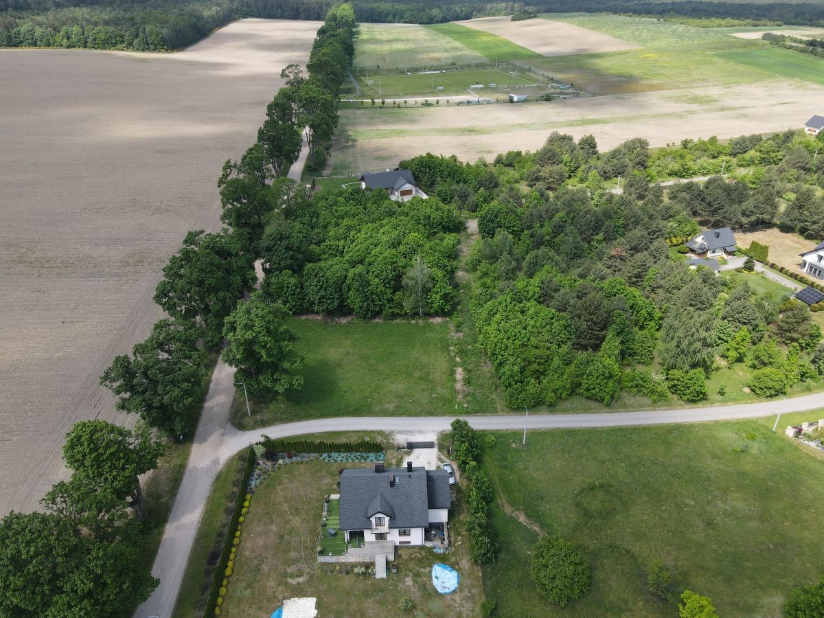 Aerial view of a rural property with houses tucked among dense trees and surrounding fields, a road running through the scene.