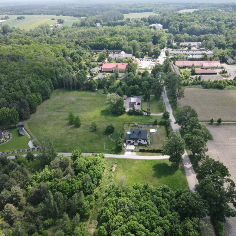 Aerial view of a rural area with fields, roads, and dense clusters of trees surrounding scattered houses and farm buildings.