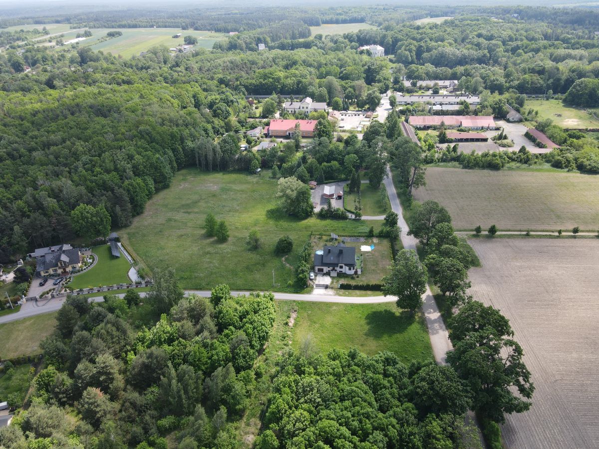 Aerial view of a rural area with fields, roads, and dense clusters of trees surrounding scattered houses and farm buildings.