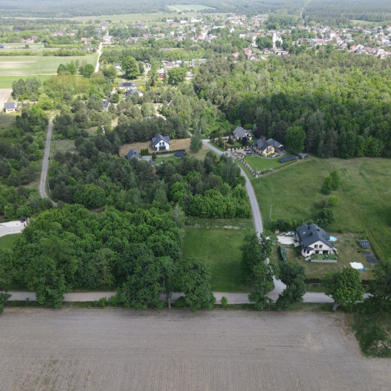 Aerial view of a rural neighborhood with houses amid dense trees and open fields, a curved road cutting through the greenery.