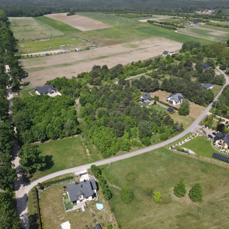 Aerial view of a rural neighborhood with houses, trees, and surrounding fields along a curved road with farmland beyond.
