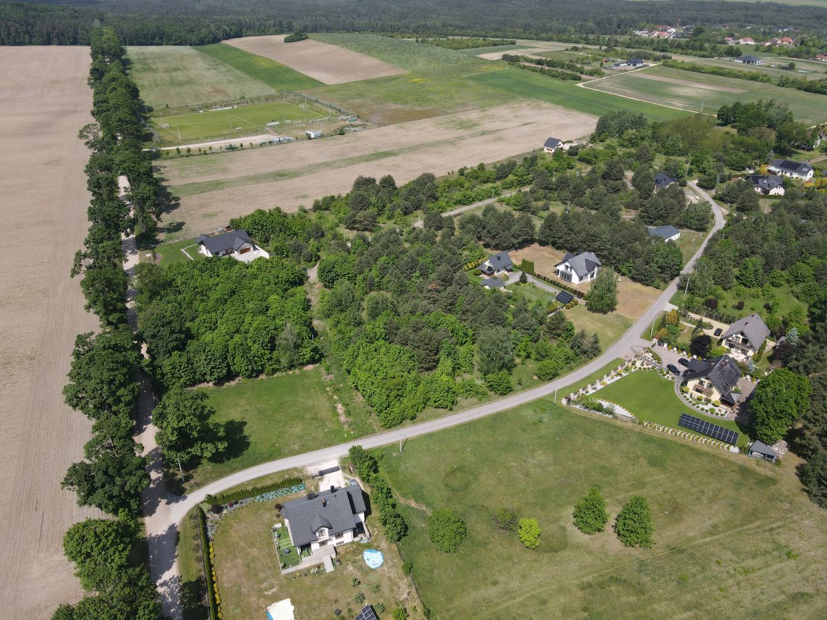 Aerial view of a rural neighborhood with houses, trees, and surrounding fields along a curved road with farmland beyond.