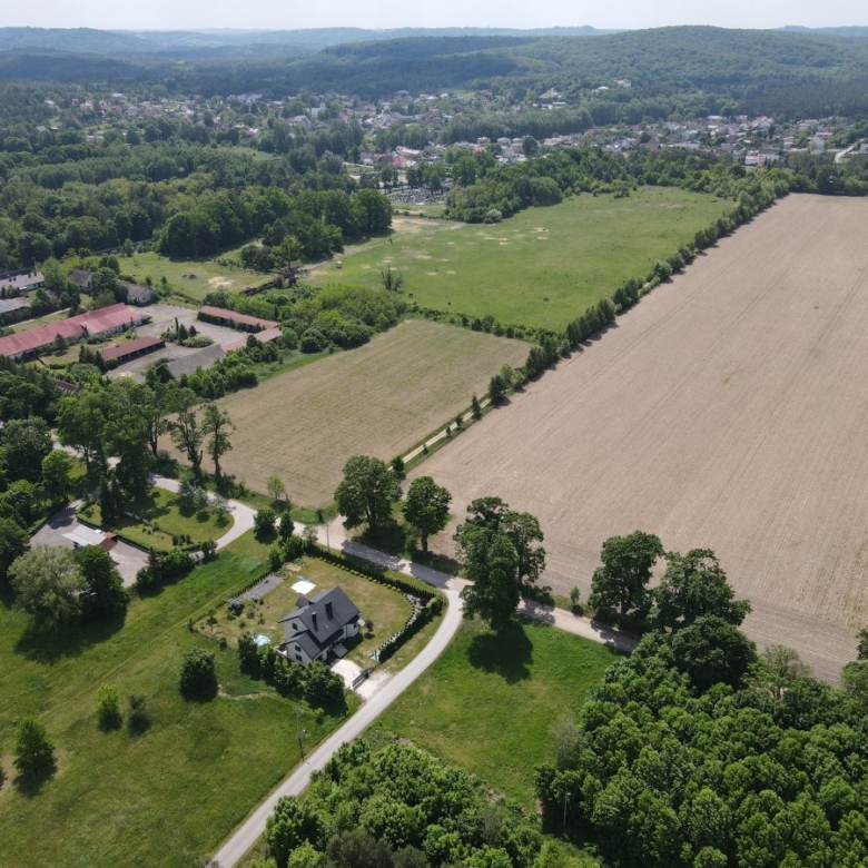 Aerial view of a rural landscape with fields, trees, and a winding road surrounding a house and small neighborhood.