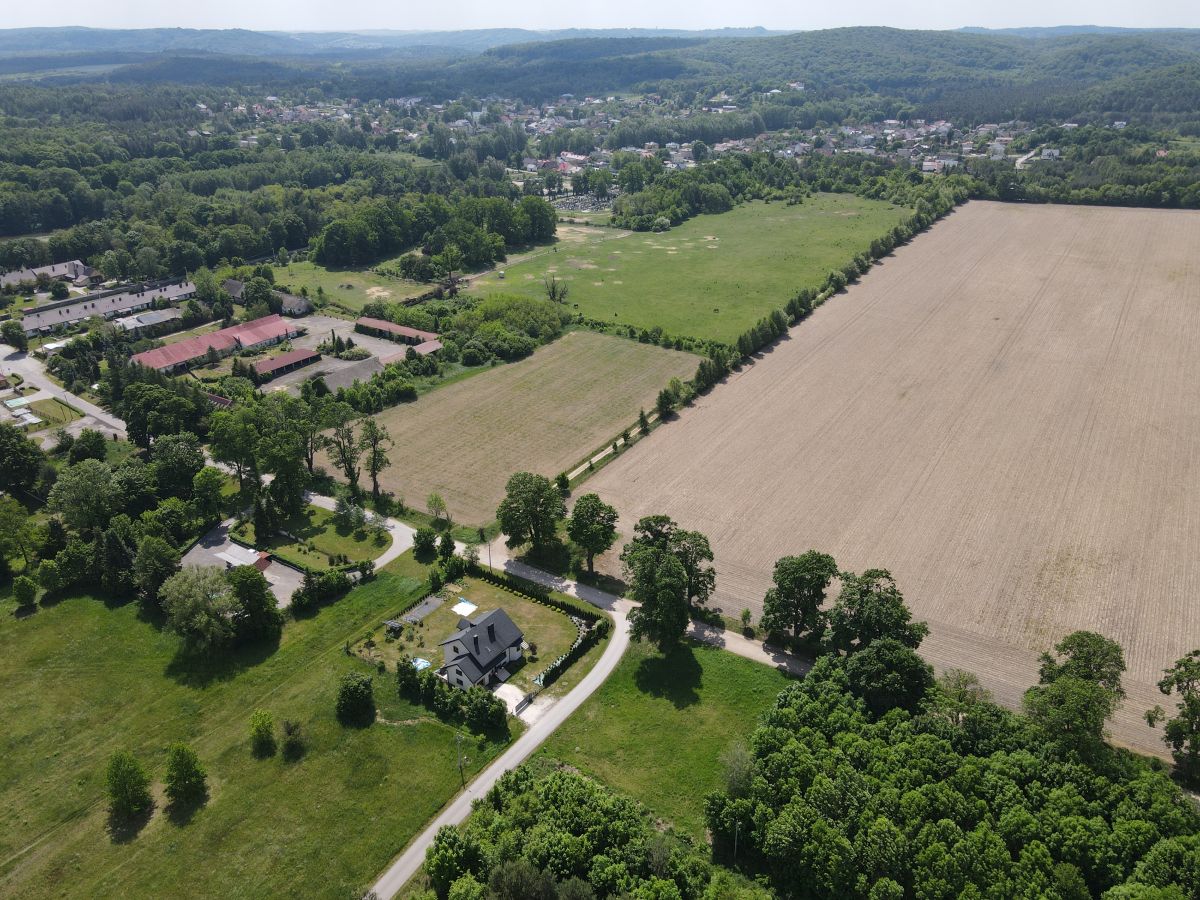Aerial view of a rural landscape with fields, trees, and a winding road surrounding a house and small neighborhood.
