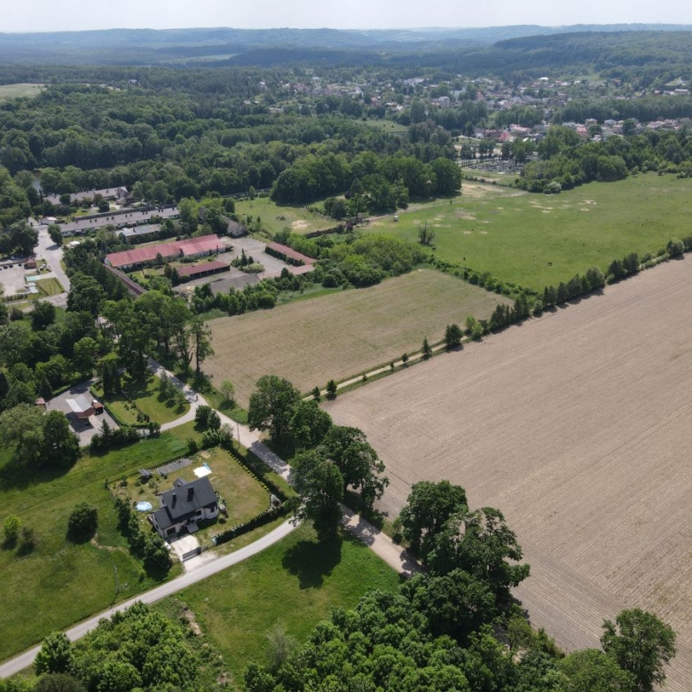 Aerial view of a rural landscape with fields, forests, and a cluster of houses along winding roads under a clear sky