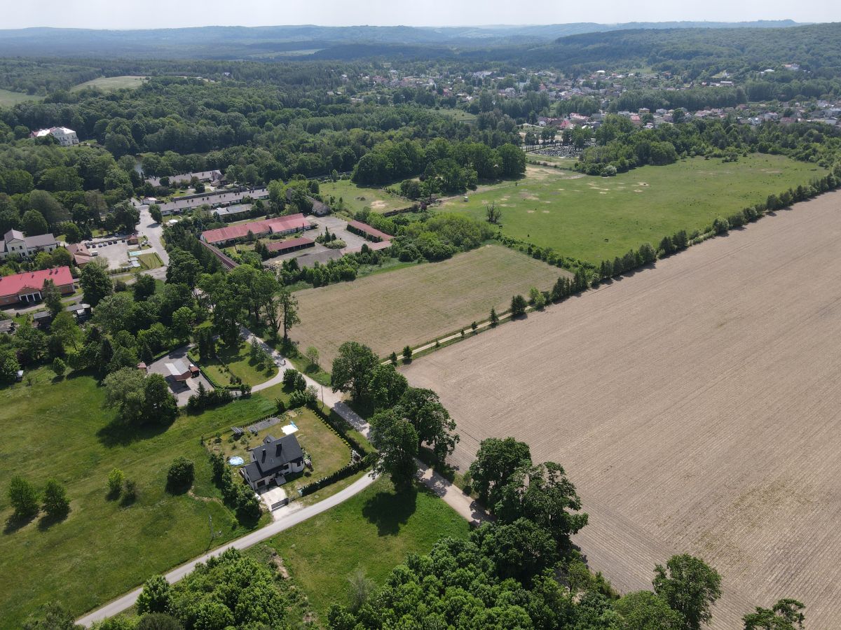 Aerial view of a rural landscape with fields, forests, and a cluster of houses along winding roads under a clear sky