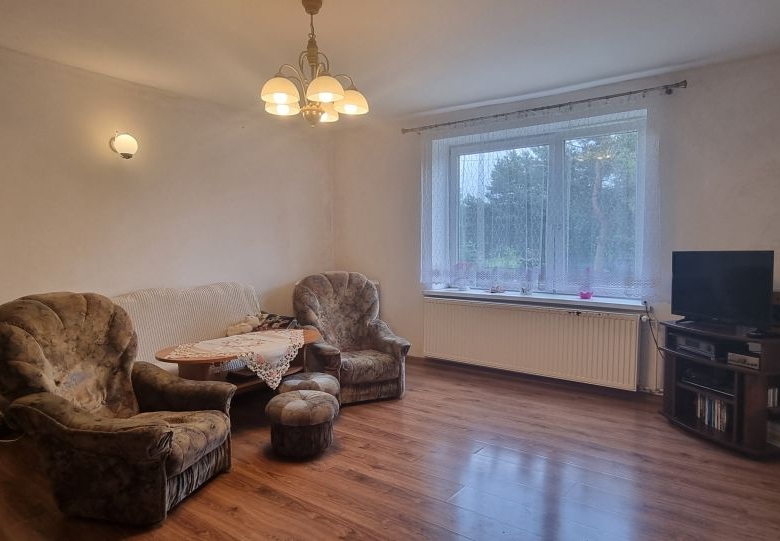 Cozy living room with two upholstered armchairs around a small round table, a floor lamp, and a TV on a wooden stand by a large window.