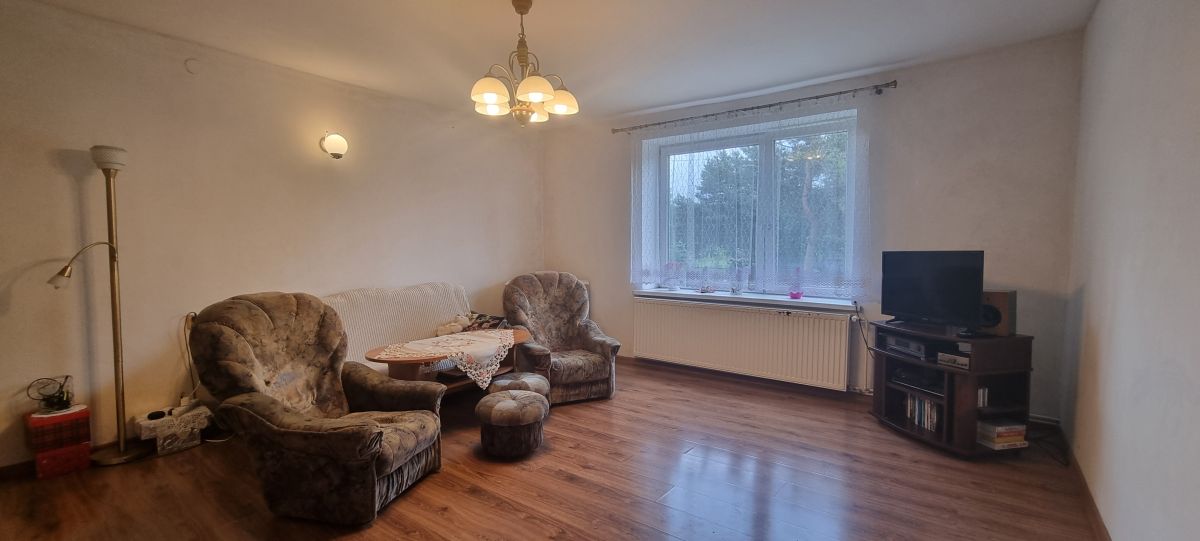 Cozy living room with two upholstered armchairs around a small round table, a floor lamp, and a TV on a wooden stand by a large window.