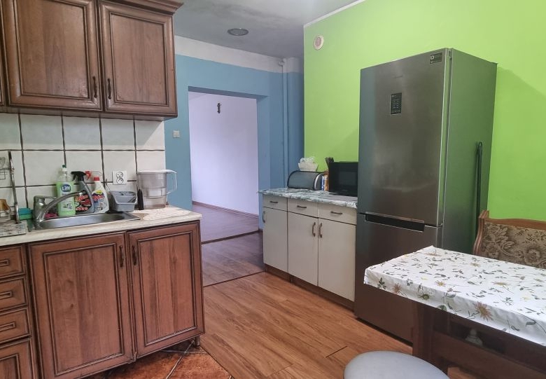 Kitchen with dark wood cabinets, a stainless refrigerator, and a dining table with a floral tablecloth against a bright green wall.