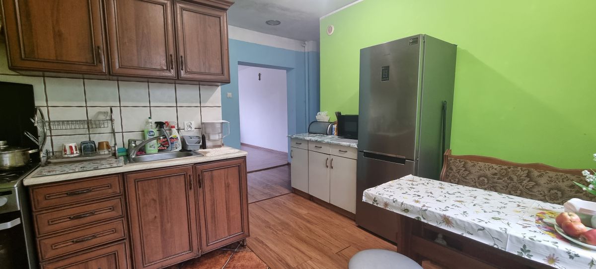 Kitchen with dark wood cabinets, a stainless refrigerator, and a dining table with a floral tablecloth against a bright green wall.