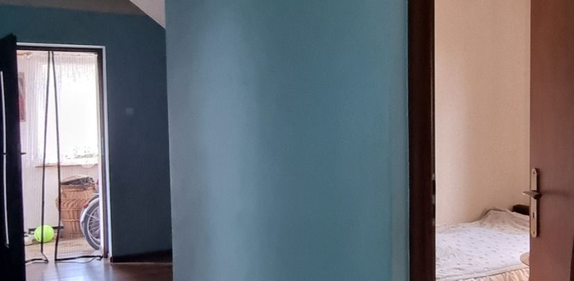 Blue-painted hallway wall with a doorway to a bedroom on the right; a left room shows a window, a bicycle wheel, and a green ball on the floor.