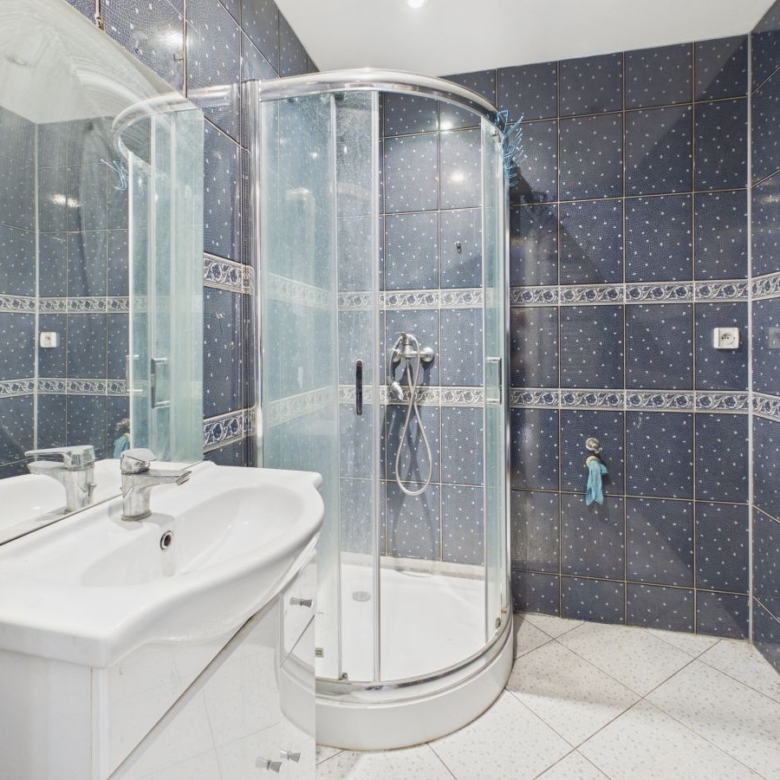 Blue tiled bathroom with a curved glass shower enclosure and white sink vanity.