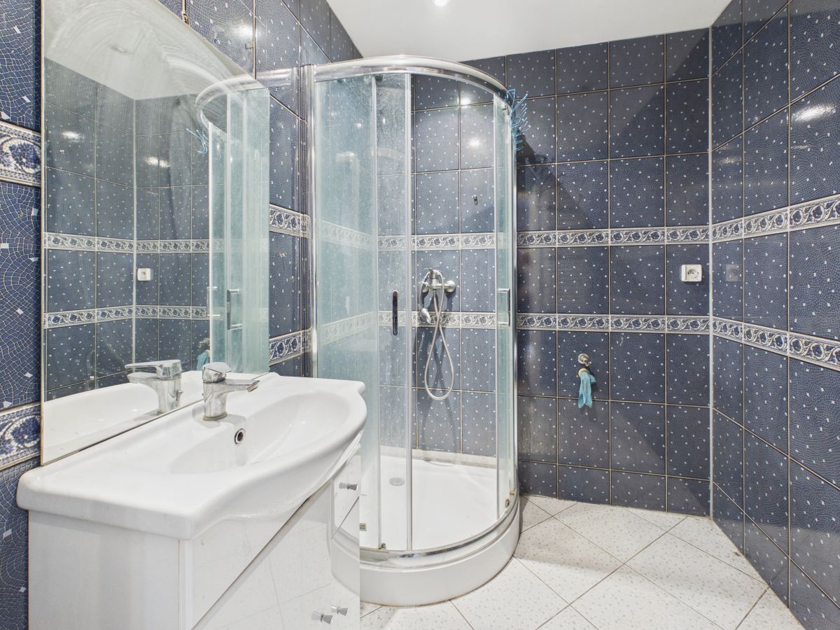 Blue tiled bathroom with a curved glass shower enclosure and white sink vanity.