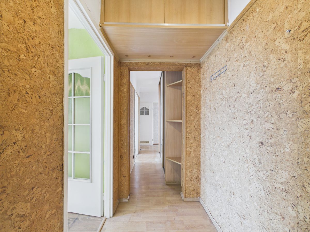 Narrow hallway with OSB walls, open doorway to a room, and built-in shelves along one side; light wood flooring and ceiling panels create a warm, unfinished look.