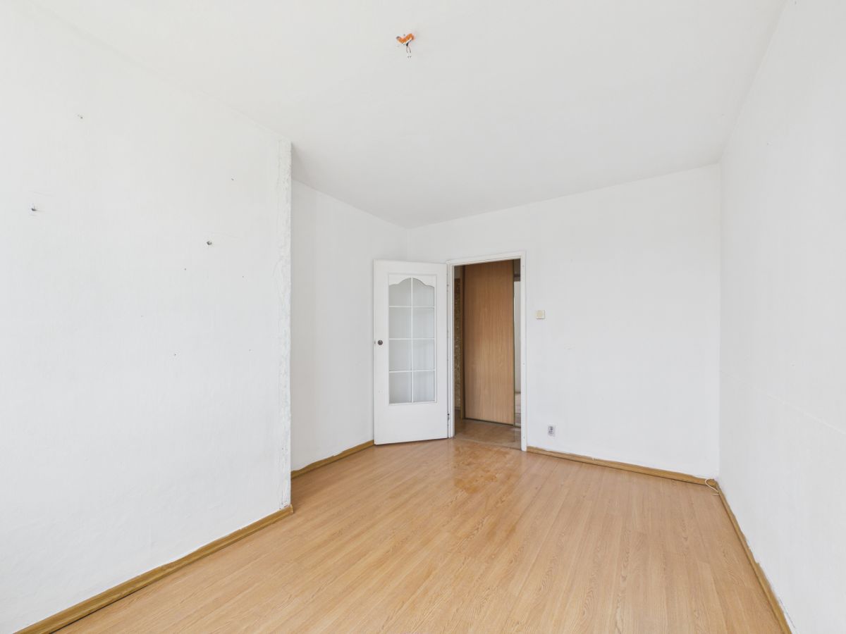 Empty white room with a light wood floor and an open door with glass panels leading to another room.