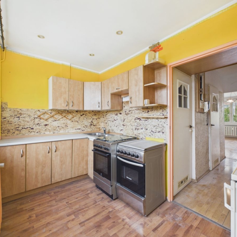 Bright yellow kitchen with wooden cabinets, a granite backsplash, and a stainless steel stove/oven; doorway to adjoining room visible.