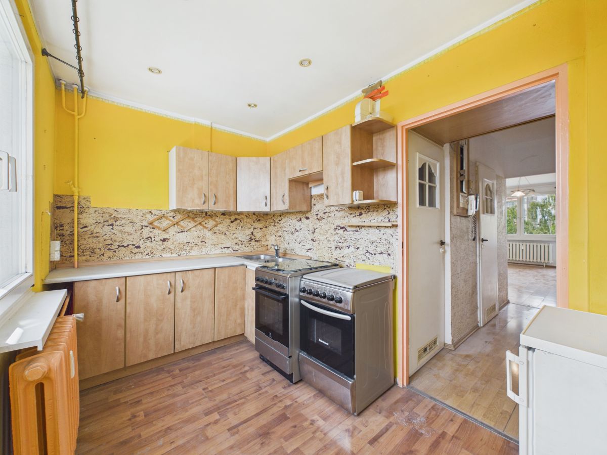 Bright yellow kitchen with wooden cabinets, a granite backsplash, and a stainless steel stove/oven; doorway to adjoining room visible.