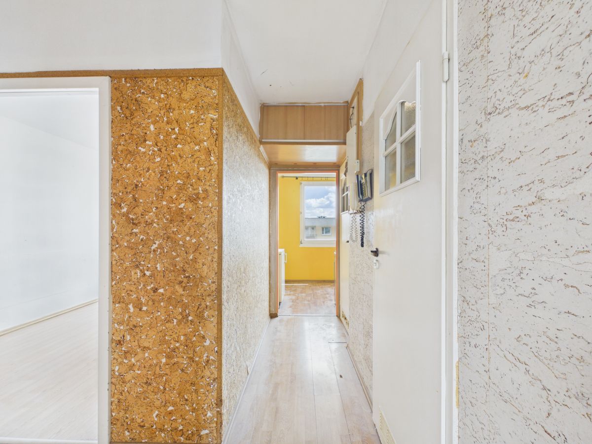 Narrow hallway in a retro apartment with cork walls, white doors, and a bright yellow room visible at the far end through an open door.