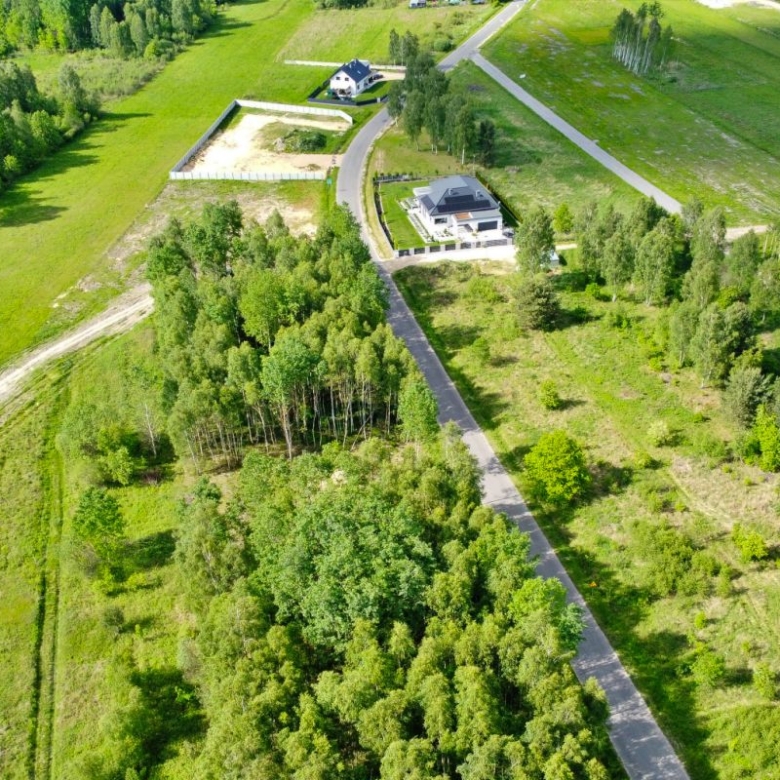 Aerial view of a rural estate with a long driveway to a house, fenced yard, and surrounding green fields and trees.