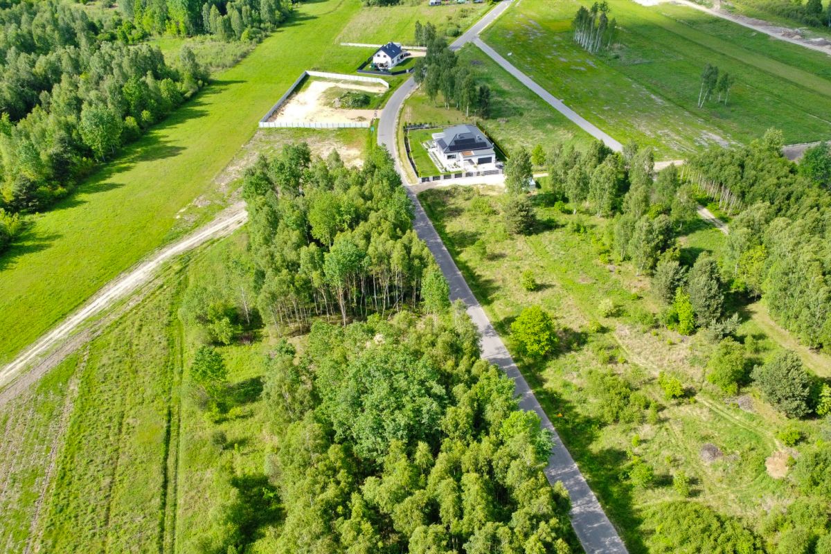 Aerial view of a rural estate with a long driveway to a house, fenced yard, and surrounding green fields and trees.