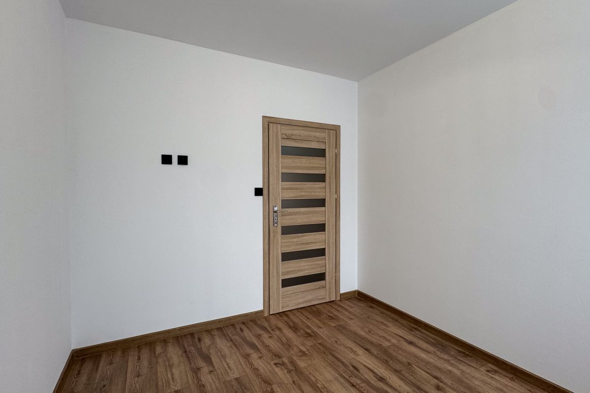 Empty white-walled room with a wooden door that has horizontal frosted-glass panels and a wood floor.