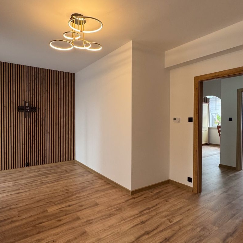 Empty living room with a vertical wood slat accent wall, warm hardwood floor, and a circular modern chandelier.