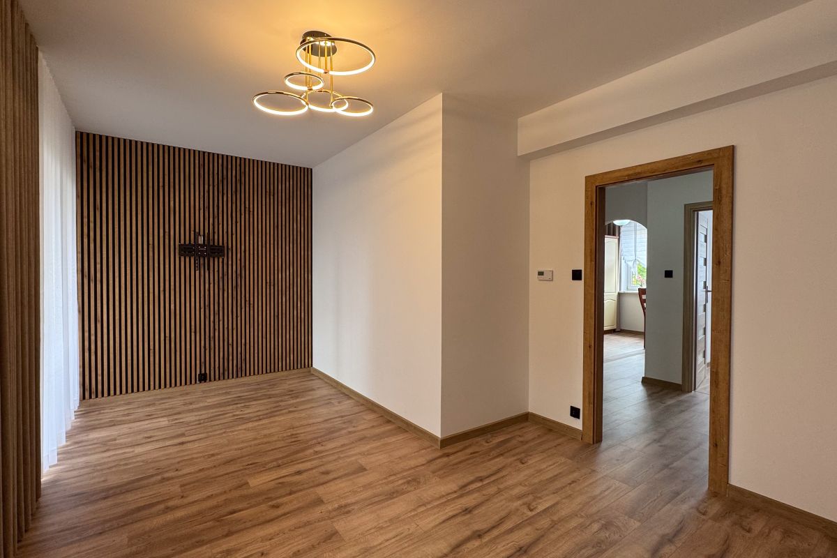 Empty living room with a vertical wood slat accent wall, warm hardwood floor, and a circular modern chandelier.