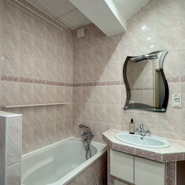 Pink-tiled bathroom with a white bathtub, oval sink vanity, decorative curved mirror, and a washing machine in the corner.