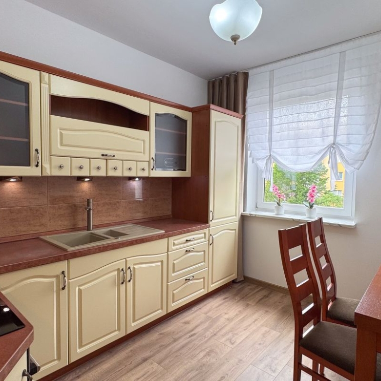 Cozy kitchen with cream cabinets, brown countertops, double sink, and a wooden dining table by a window with sheer curtains.