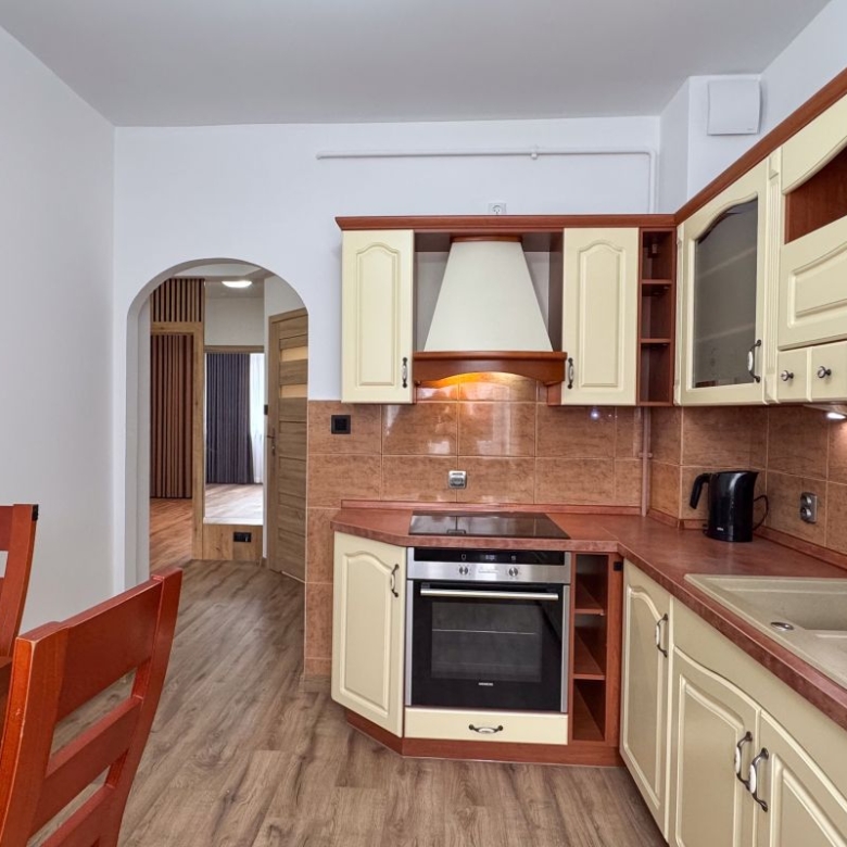 Cream kitchen with brown countertops and backsplash, built-in oven and stovetop, range hood, and double sink; wooden dining table in foreground.