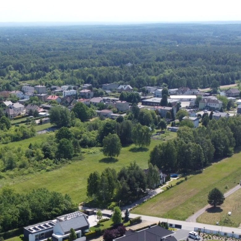 Aerial view of a small town with houses, roads and green fields bordered by trees and dense forest in the distance.