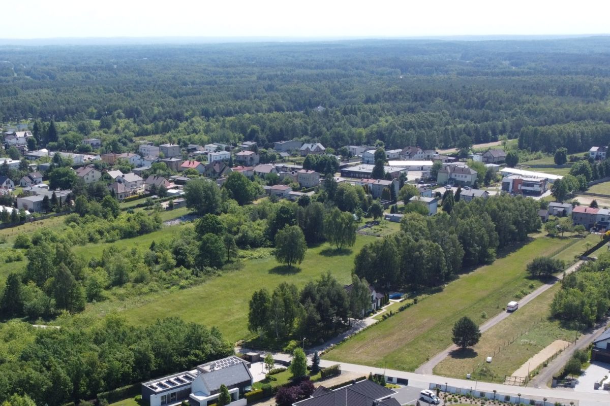 Aerial view of a small town with houses, roads and green fields bordered by trees and dense forest in the distance.