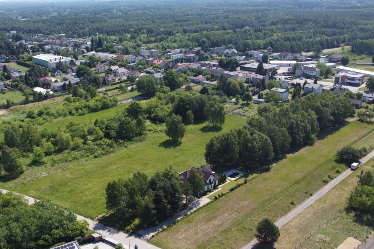 Aerial view of a rural town with houses, green fields and tree-lined streets.