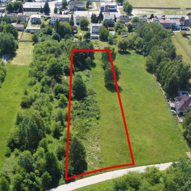 Aerial view of a vacant lot outlined in red in a green residential area, with trees along the edges and nearby houses.