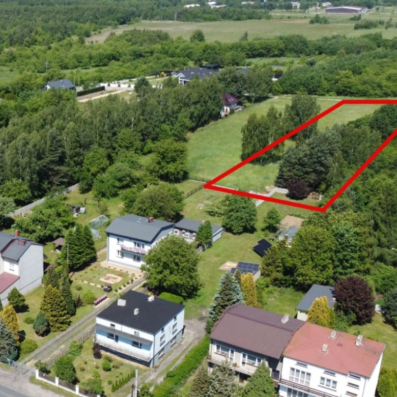 Aerial view of a residential area with a large grassy plot outlined in red, bordered by trees and houses nearby.