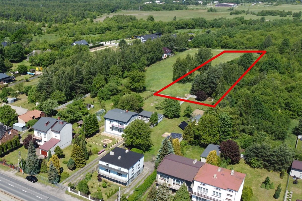 Aerial view of a residential area with a large grassy plot outlined in red, bordered by trees and houses nearby.