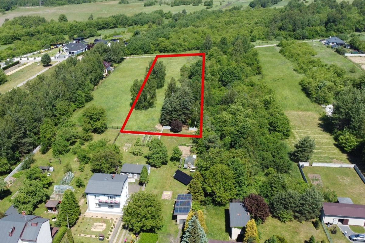 Aerial view of a rectangular plot of grassy land outlined in red, bordered by trees and neighboring properties in a suburban area.