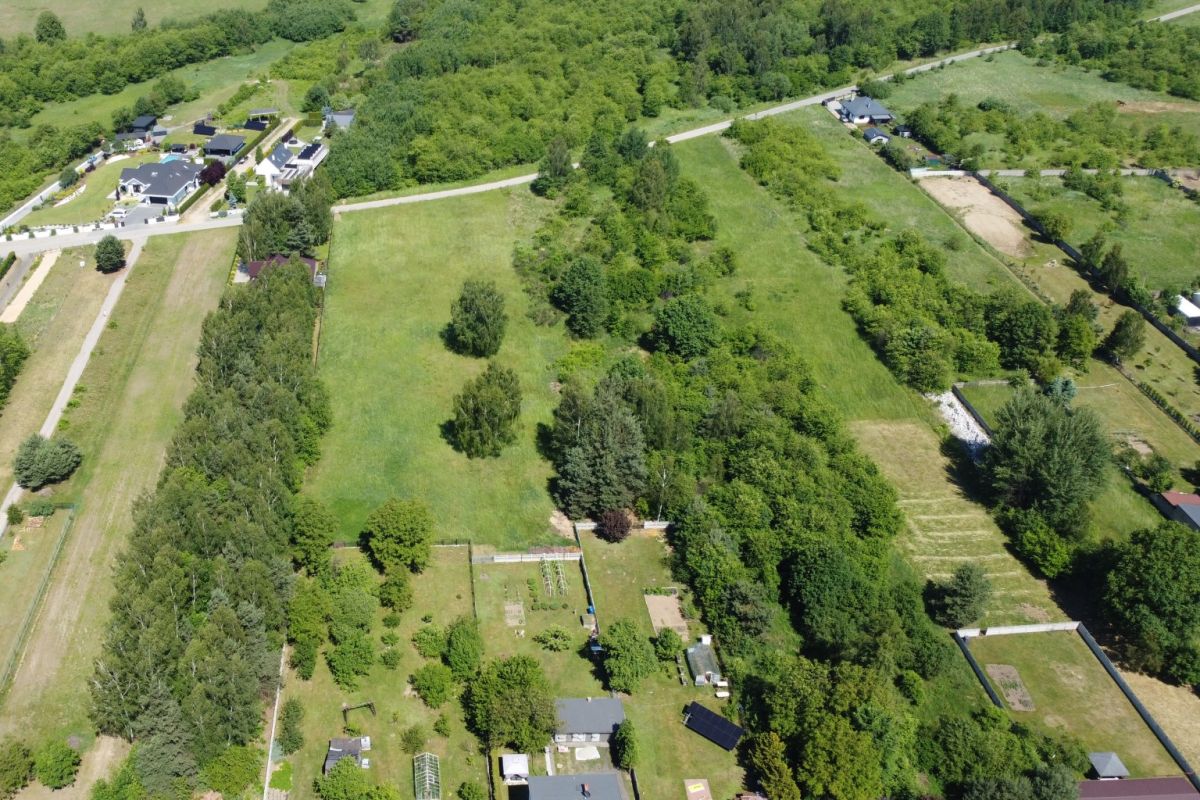 Aerial view of a green rural landscape with fields, trees, and scattered houses along winding roads.