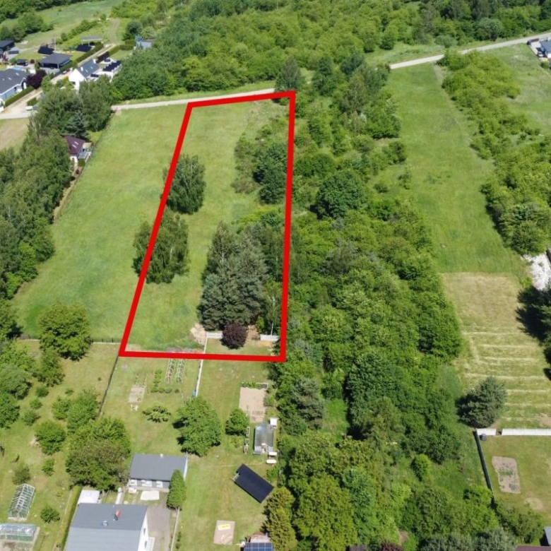 Aerial view of a rectangular green lot outlined in red, with trees along the edges and houses nearby in a suburban area.