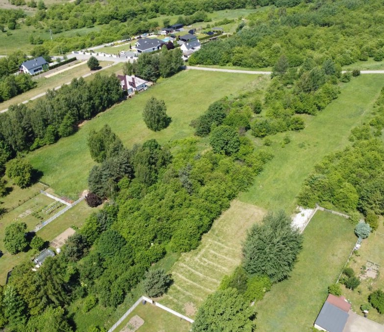 Aerial view of a green rural area with open fields, tree lines, and scattered houses along roads.