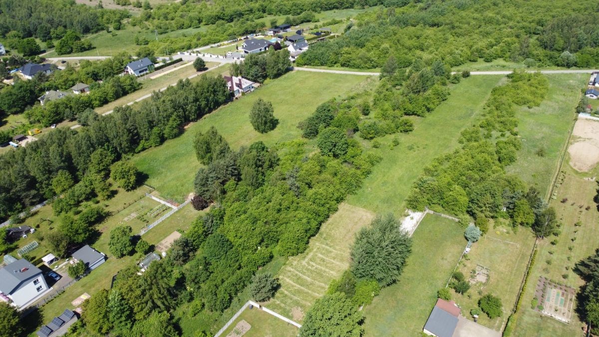 Aerial view of a green rural area with open fields, tree lines, and scattered houses along roads.