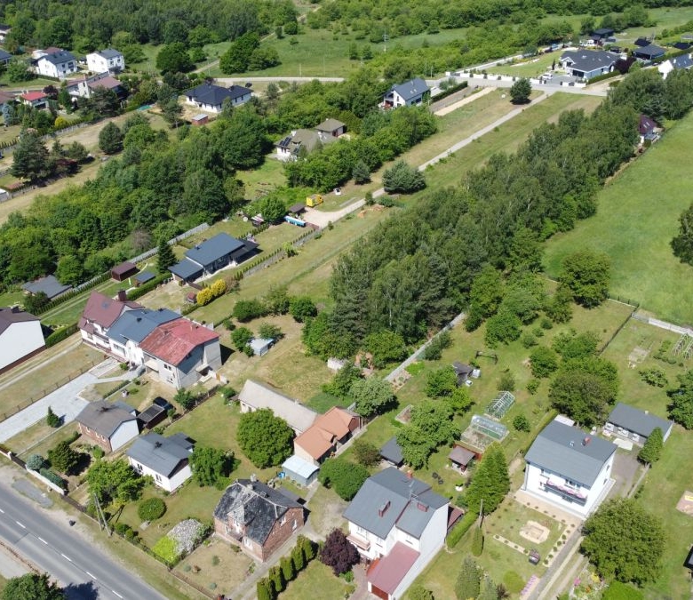 Aerial view of a residential neighborhood with houses, trees, and a large green field bordered by roads and fences.